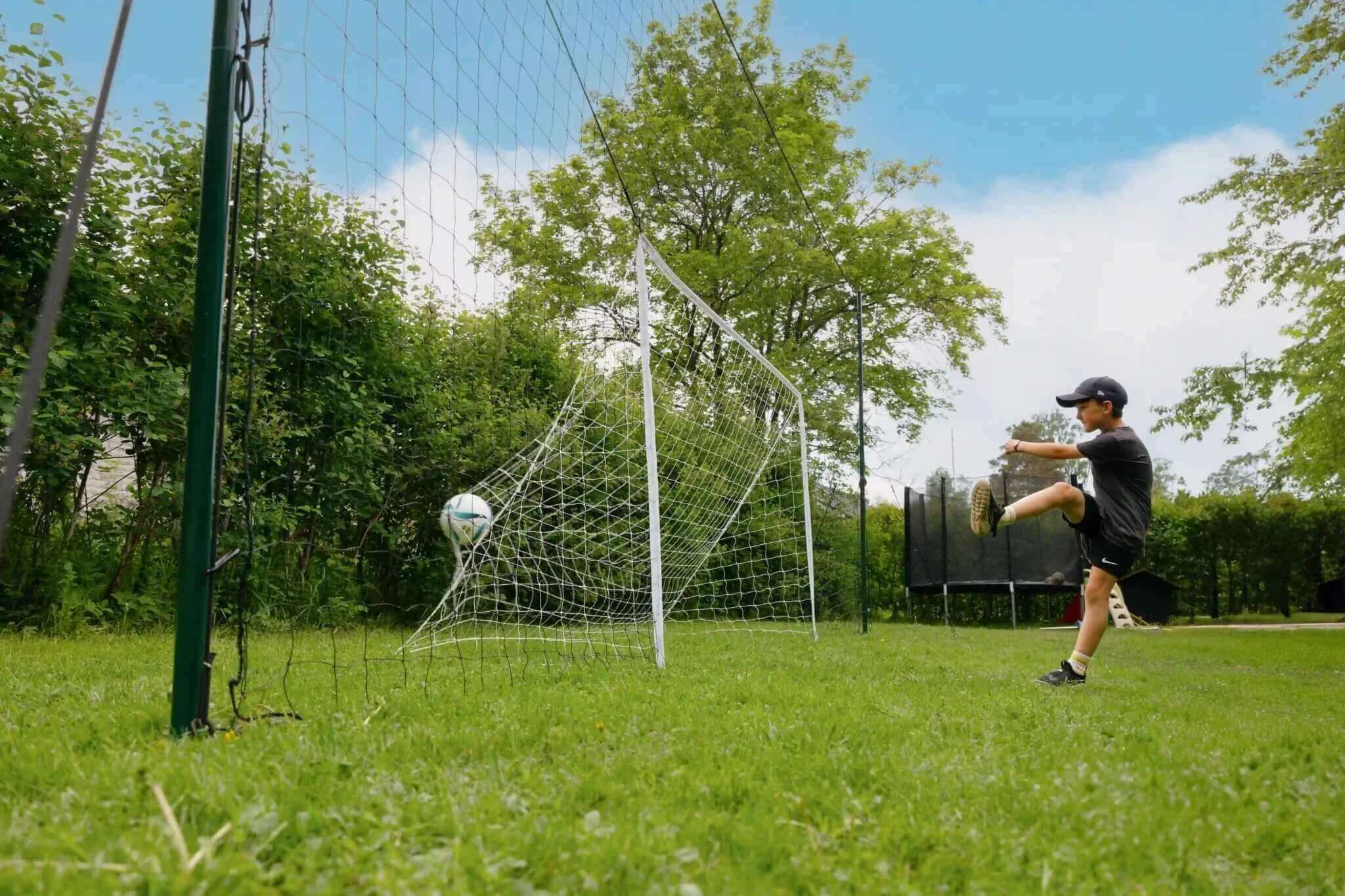 Child practicing football kick with 3-in-1 Football Goal Trainer rebounder and goal in backyard