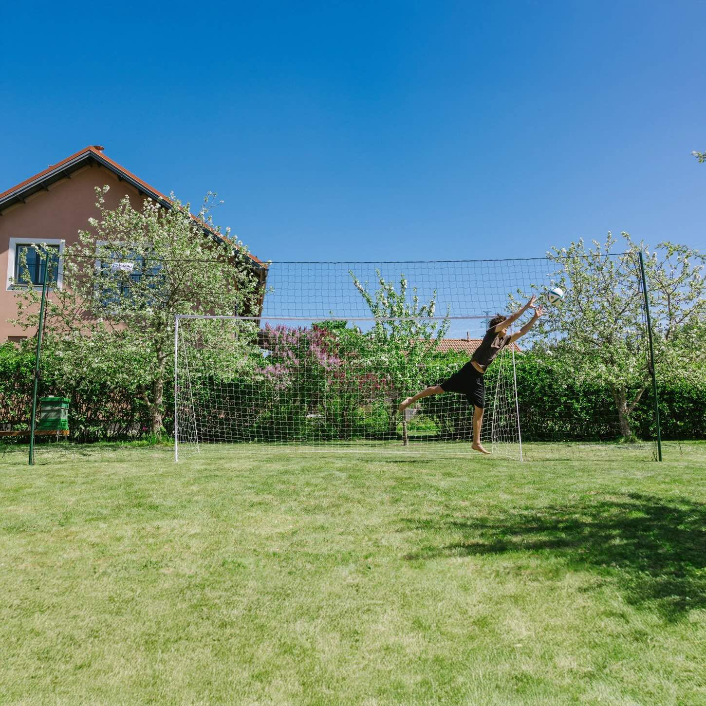 Goalkeeper diving to save a shot in an Open Goaaal Large football goal with backstop netting in a garden