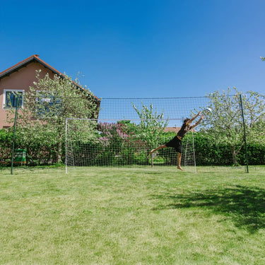 Goalkeeper diving to save a shot in an Open Goaaal Large football goal with backstop netting in a garden